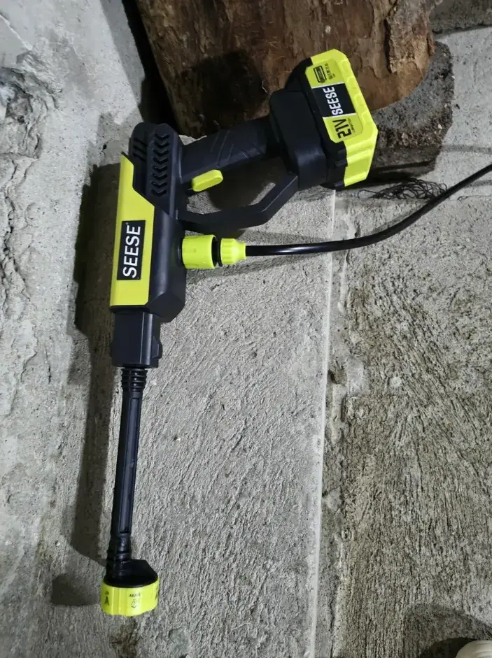 Lavadora montada com bateria, lança e mangueira sobre o piso de concreto da garagem